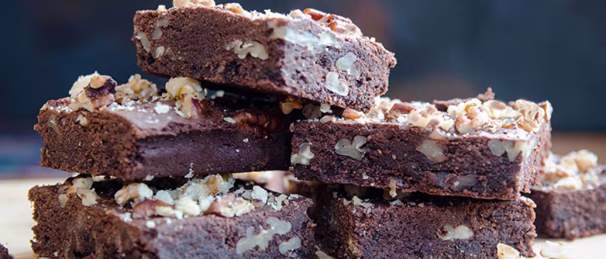 A stack of chocolate and pecan brownies, sprinkled with pecan crumbs and crushed walnut, fresh out of the oven